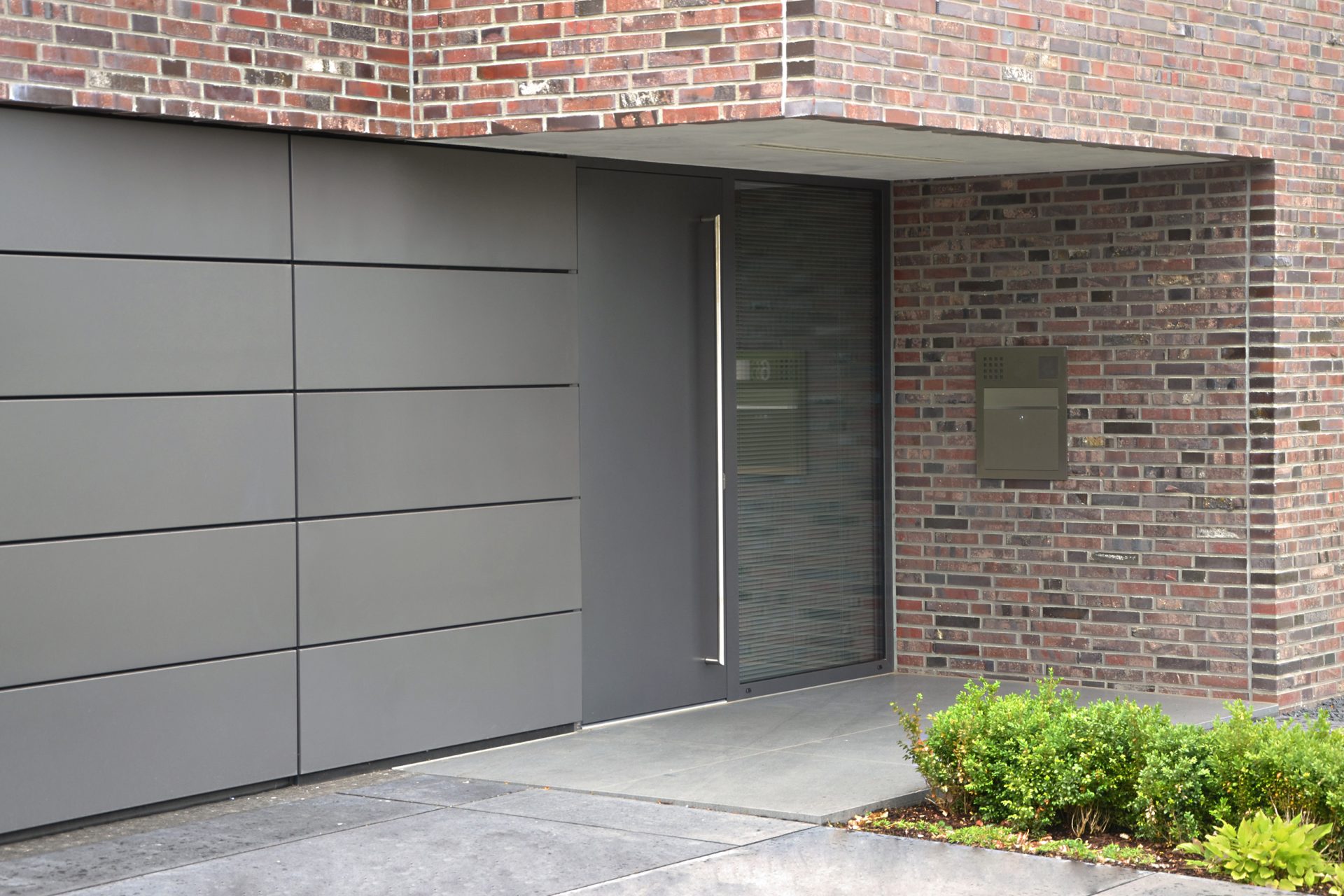 Eingangsbereich eines Hauses - Teilweise rot-braun verklinkert, teilweise mit grauen Trespa-Platten verkleidet