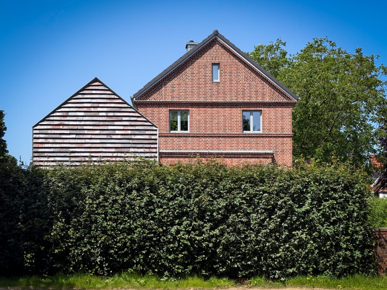 Fronatansicht auf den Anbau mit Keramikschindeln CradleTop CTP Danzig in rot-braun mit Kohleaufbrennungen und das Originalhaus
